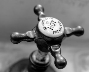 Close-up of a vintage hot water tap in black and white with visible brand details.